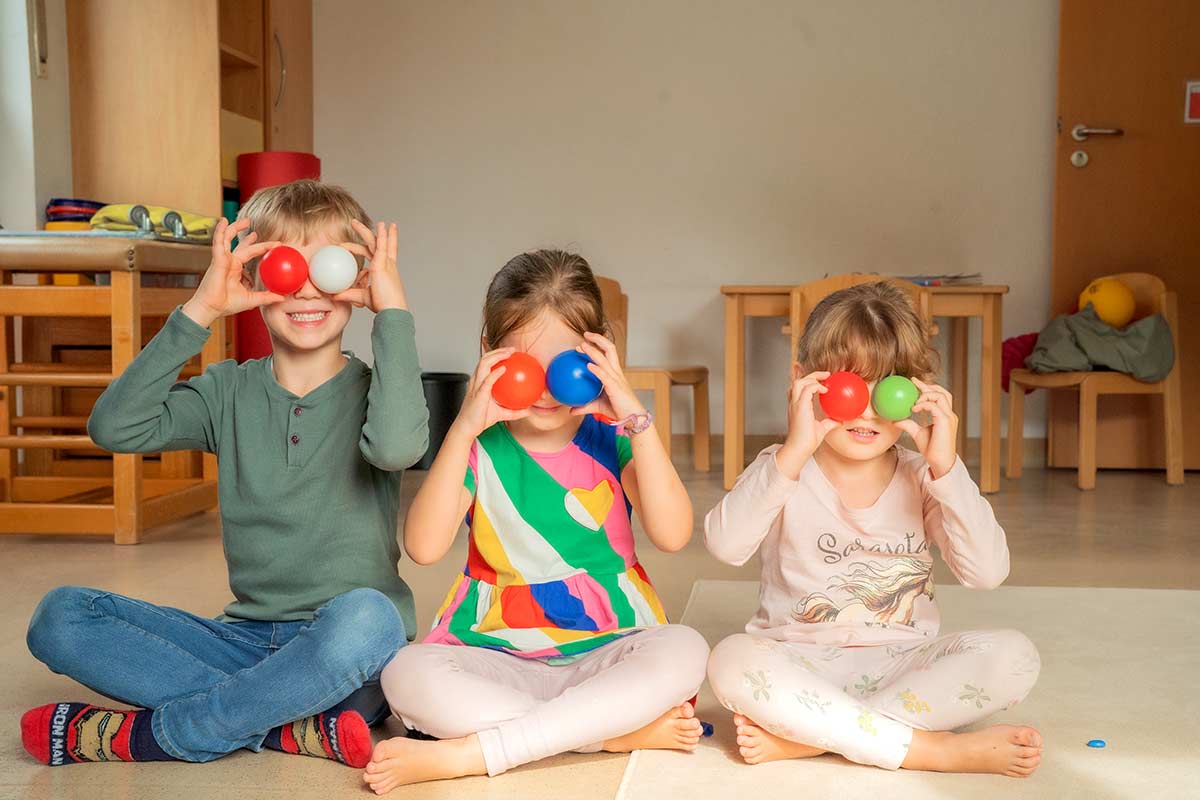 Drei Kinder halten klerine Bälle vor ihre Augen.