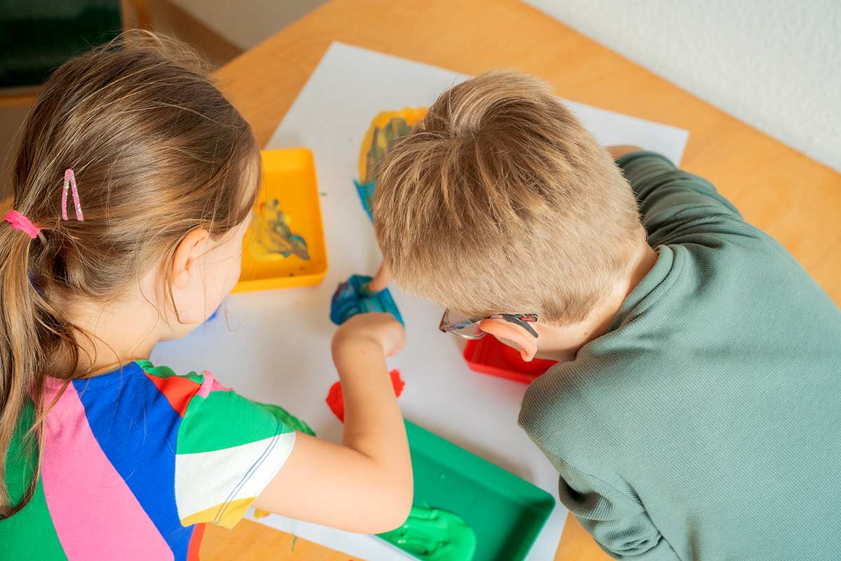 Zwei Kinder malen mit Fingerfarbe.